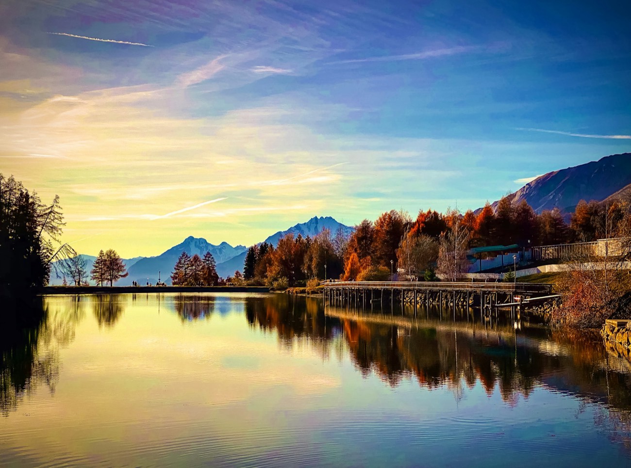 Ein See im goldenen Abendlicht, am Ufer Bäume in Herbstfarben.